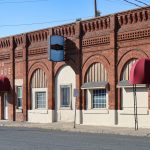 Elgin OR 29 A red brick building with arched windows and red awnings over two entrances sits along a quiet Elgin street. Signs above the doors read Garage and Creative Studios. The sidewalk is empty under clear blue skies.